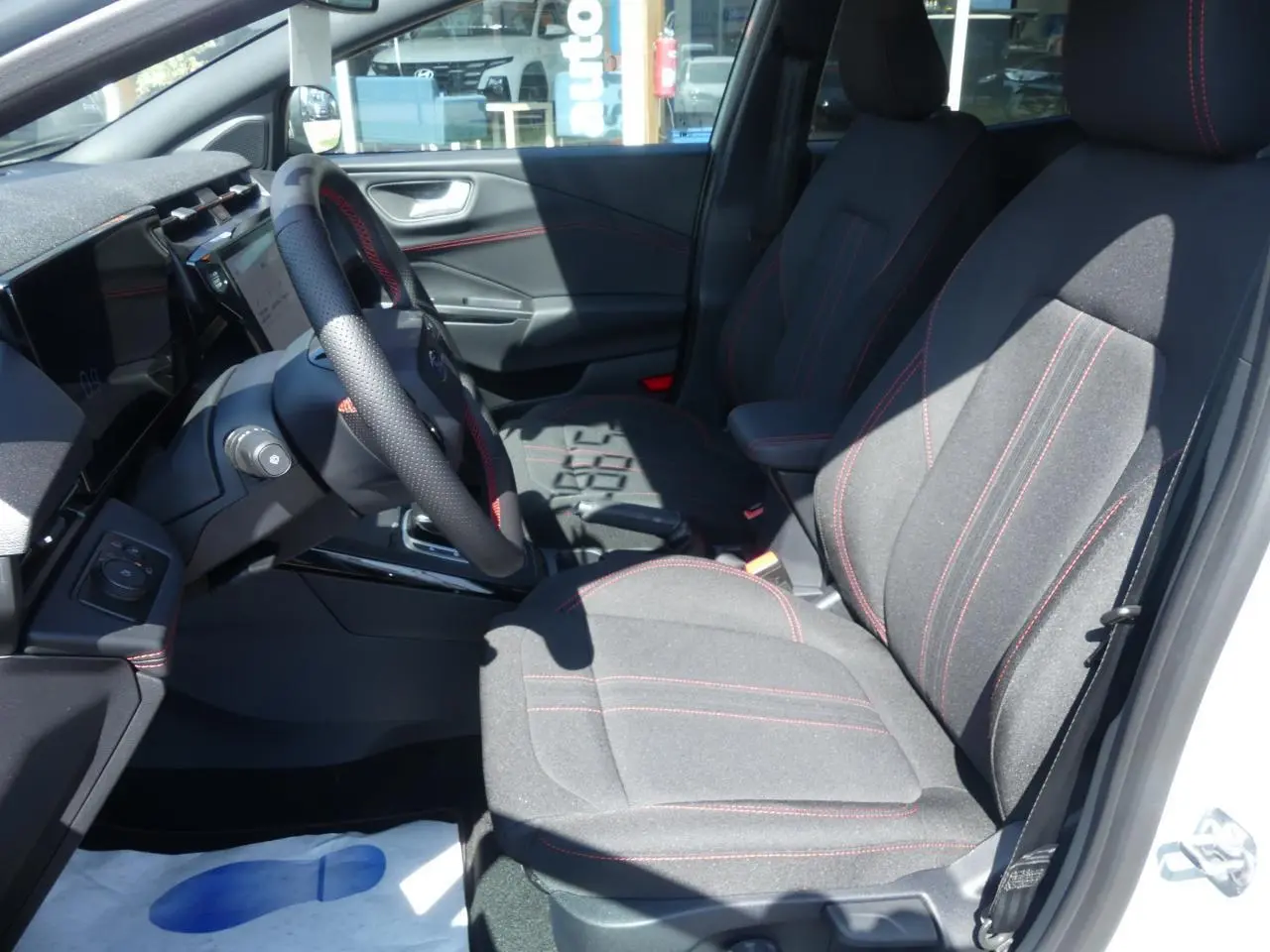 Intérieur avant droit du Ford Puma 2025 ST-Line avec sièges tissu noirs et surpiqûres rouges, volant perforé et console centrale.