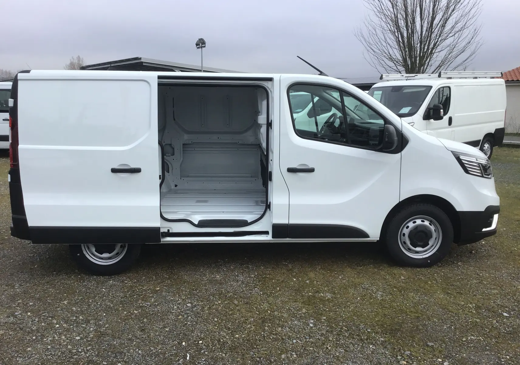 Renault Trafic Fourgon blanc vu de profil droit avec porte coulissante ouverte montrant l’espace de chargement vide.