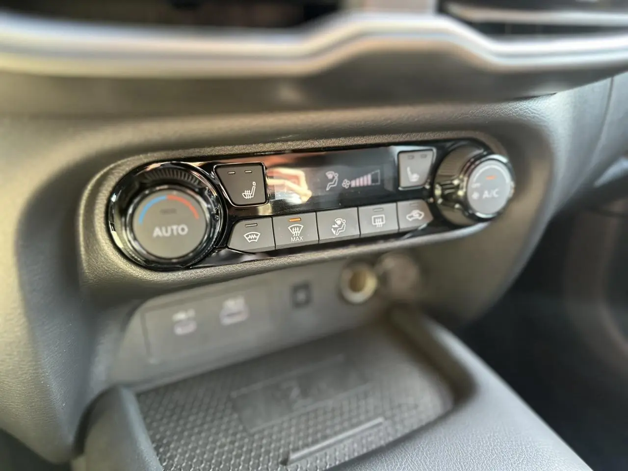 Gros plan sur la console centrale du Nissan Juke 2025 noire, montrant les commandes de climatisation automatique et sièges chauffants.