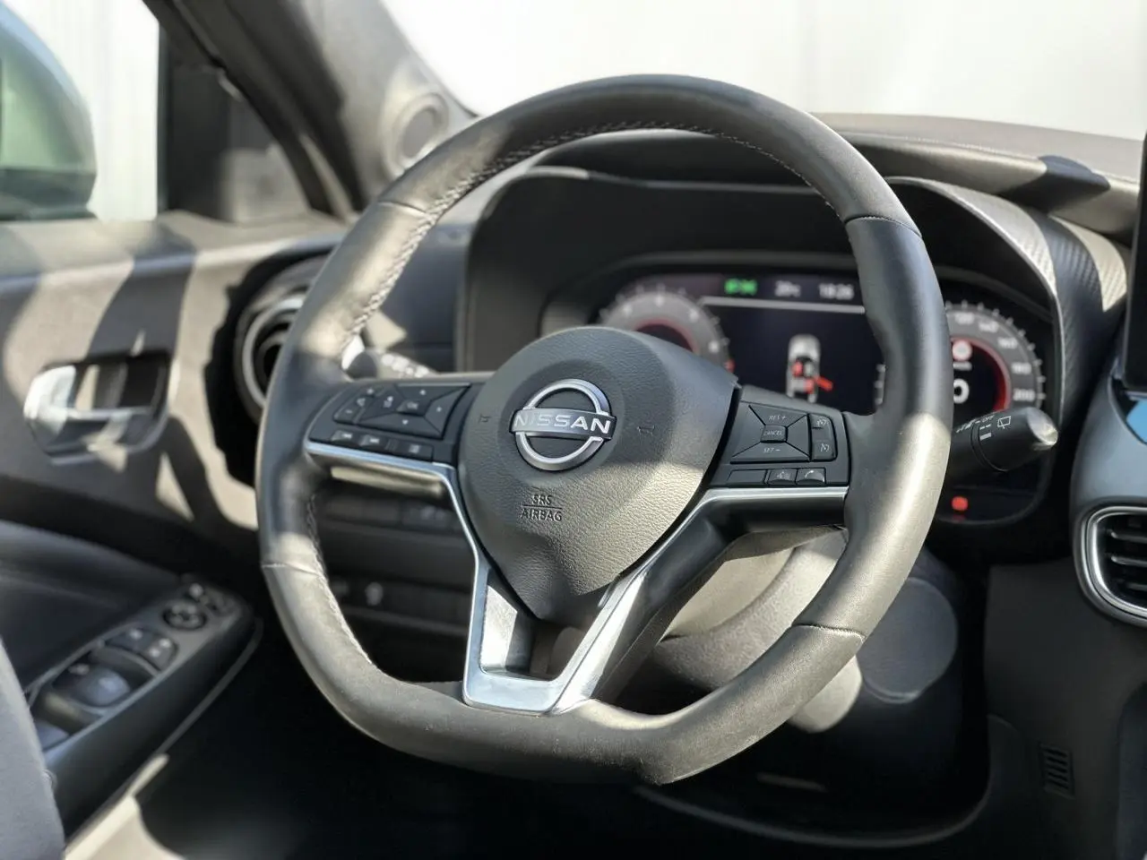 Vue rapprochée du volant en cuir noir du Nissan Juke 2025 avec commandes intégrées et tableau de bord digital en arrière-plan.