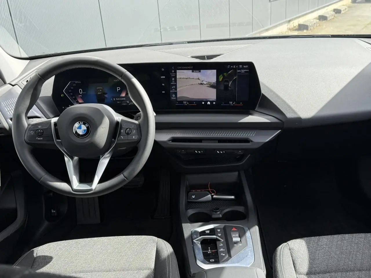 Vue intérieure avant de la BMW Série 1 118d M Sport 2025, tableau de bord noir et sièges tissu anthracite.