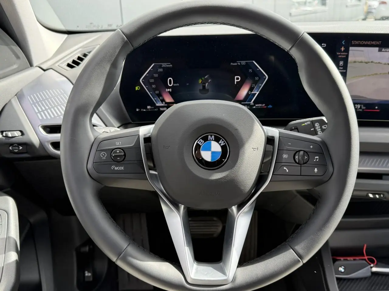 Vue rapprochée du volant noir multifonctions de la BMW Série 1 118dA 2025 avec tableau de bord numérique allumé.