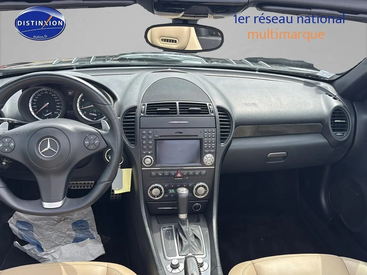 Vue intérieure du tableau de bord et console centrale d'une Mercedes SLK 55 AMG 7G-Tronic de 2009 avec sellerie cuir beige et volant noir.