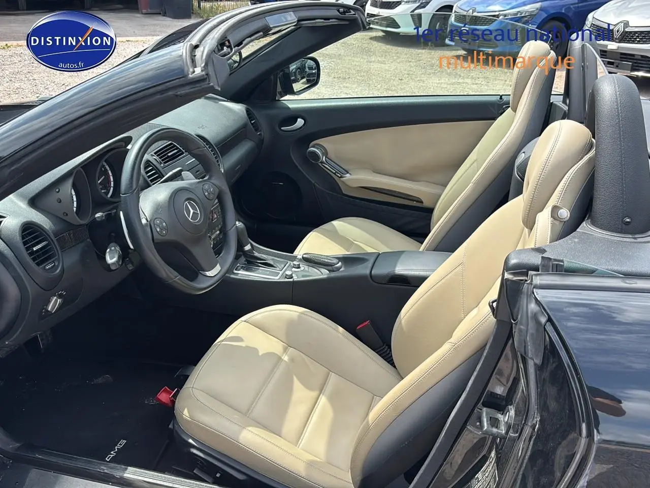 Intérieur beige clair vu côté conducteur d'une Mercedes SLK 55 AMG noire cabriolet avec volant multifonction et boîte auto.