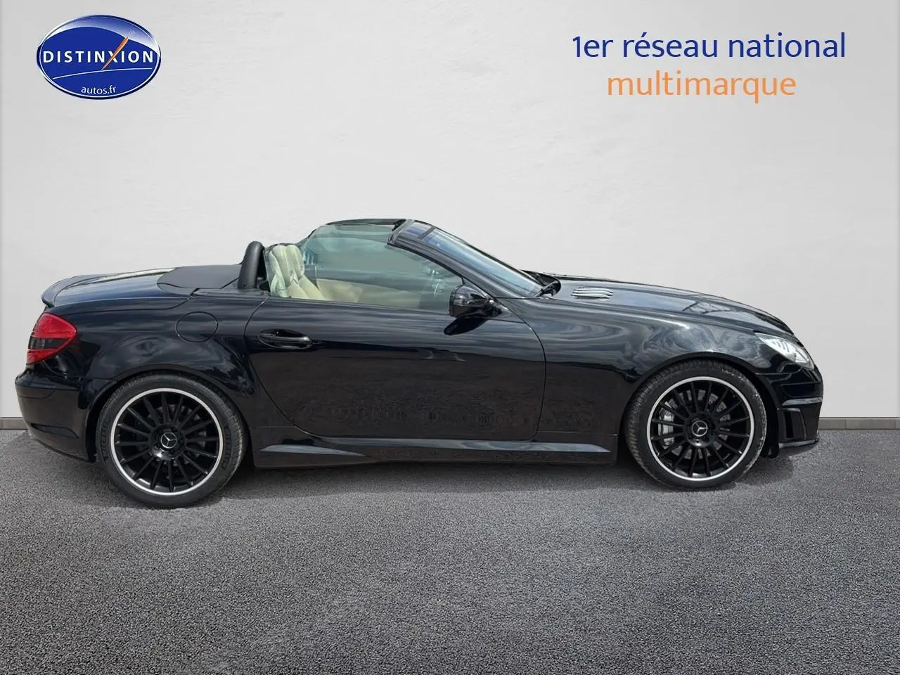 Profil côté gauche d'une Mercedes SLK 55 AMG noire cabriolet avec jantes noires et intérieur clair visible.