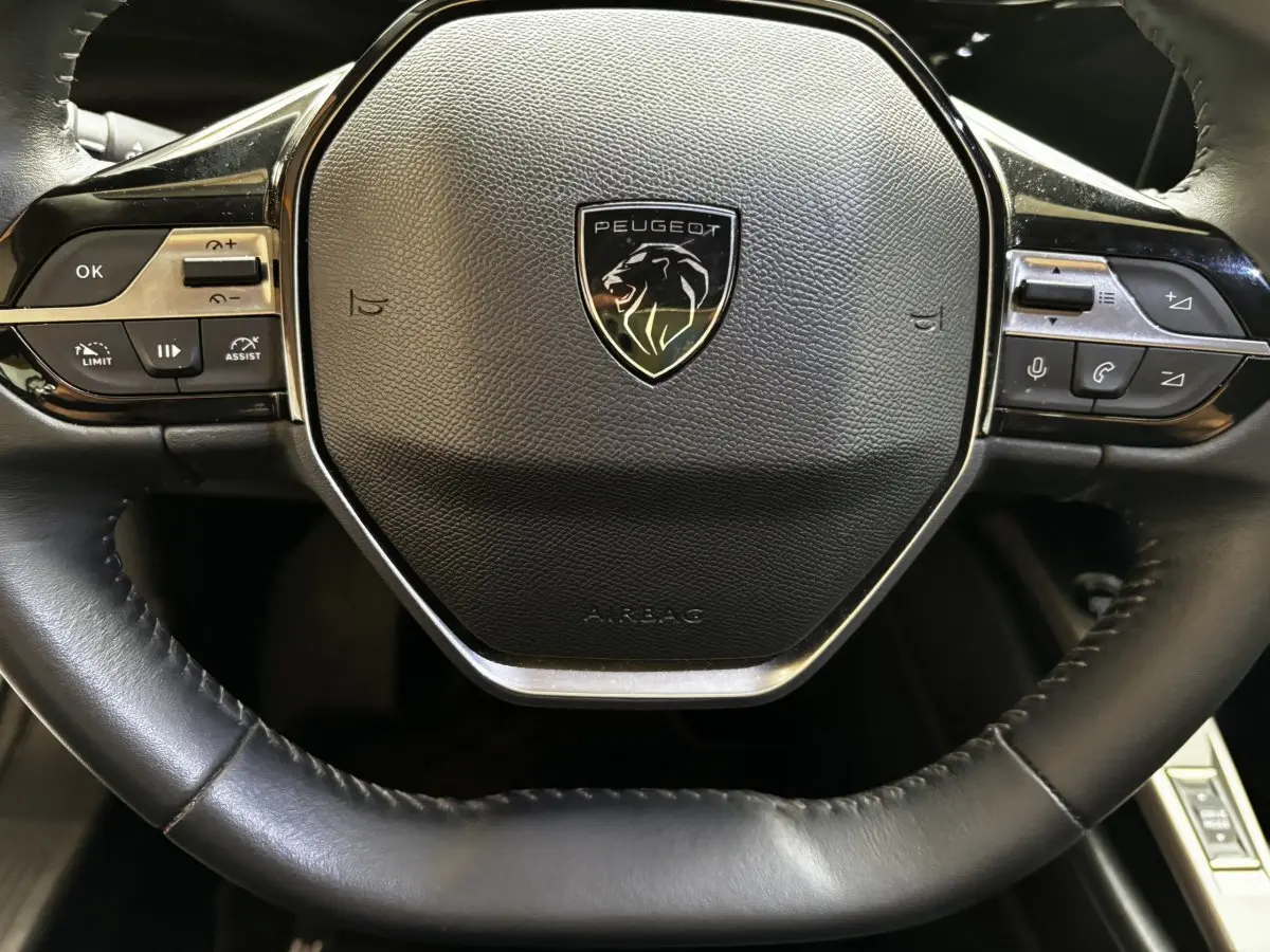 Gros plan sur le volant cuir noir de la Peugeot 308 PureTech 110 S&S ACTIVE PACK avec commandes multifonctions intégrées.
