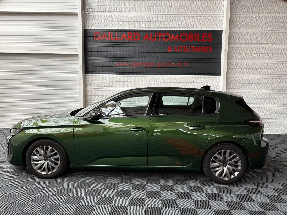 Profil côté gauche d'une Peugeot 308 vert foncé 2022 garée en intérieur avec jantes alliage et rétroviseurs noirs.