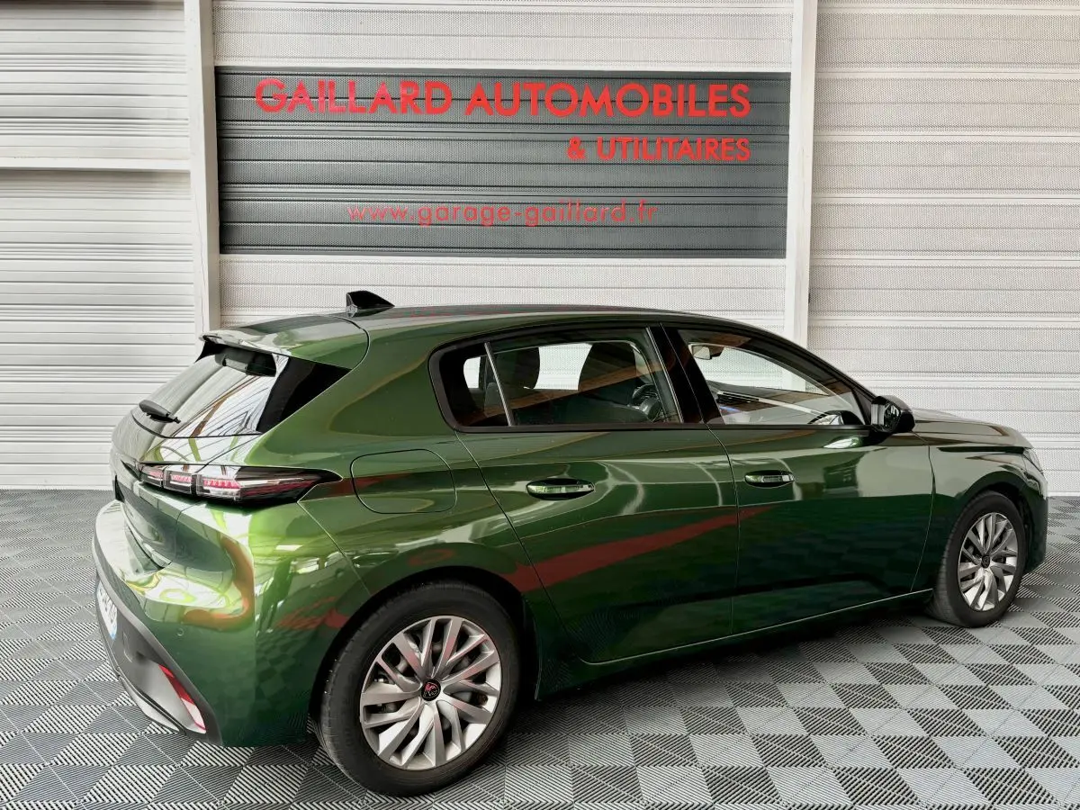 Vue 3/4 arrière droite d'une Peugeot 308 PureTech 110 S&S ACTIVE PACK verte, stationnée en intérieur sur sol damier.