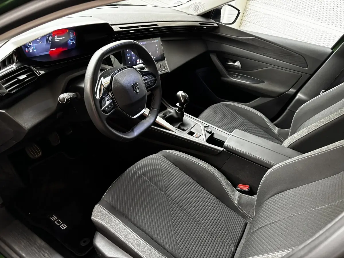 Intérieur avant droit de la Peugeot 308 2022, volant cuir, tableau de bord numérique et sièges tissu noirs.