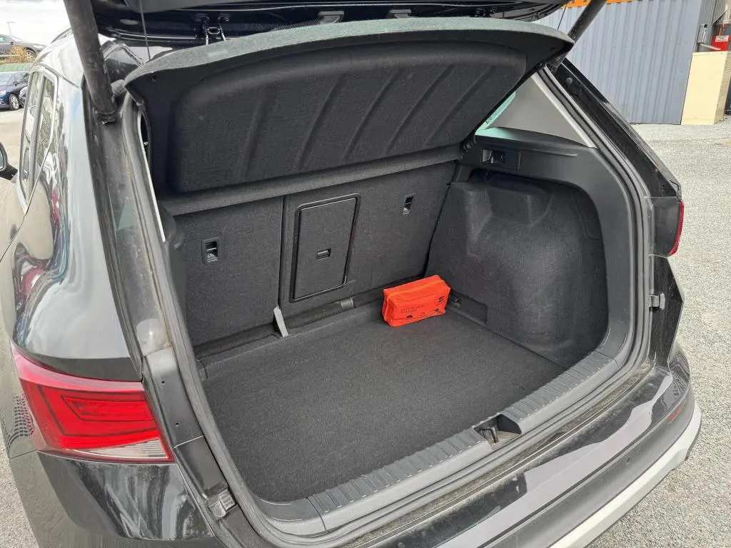 Coffre ouvert côté arrière d'un SEAT Ateca noir 2023, montrant un espace de rangement avec trappe et kit de secours rouge.