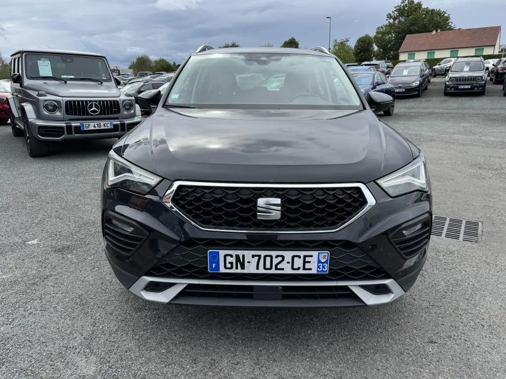 Vue frontale d'un SEAT Ateca noir métallisé avec calandre hexagonale et phares LED, sur un parking extérieur.