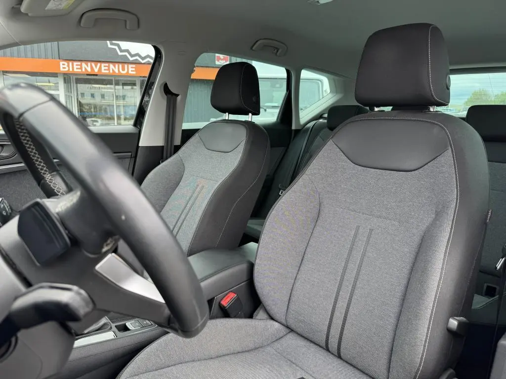 Vue intérieure sur les sièges avant en textile gris et noir du SEAT Ateca 2023, avec volant partiellement visible et arrière-plan extérieur.