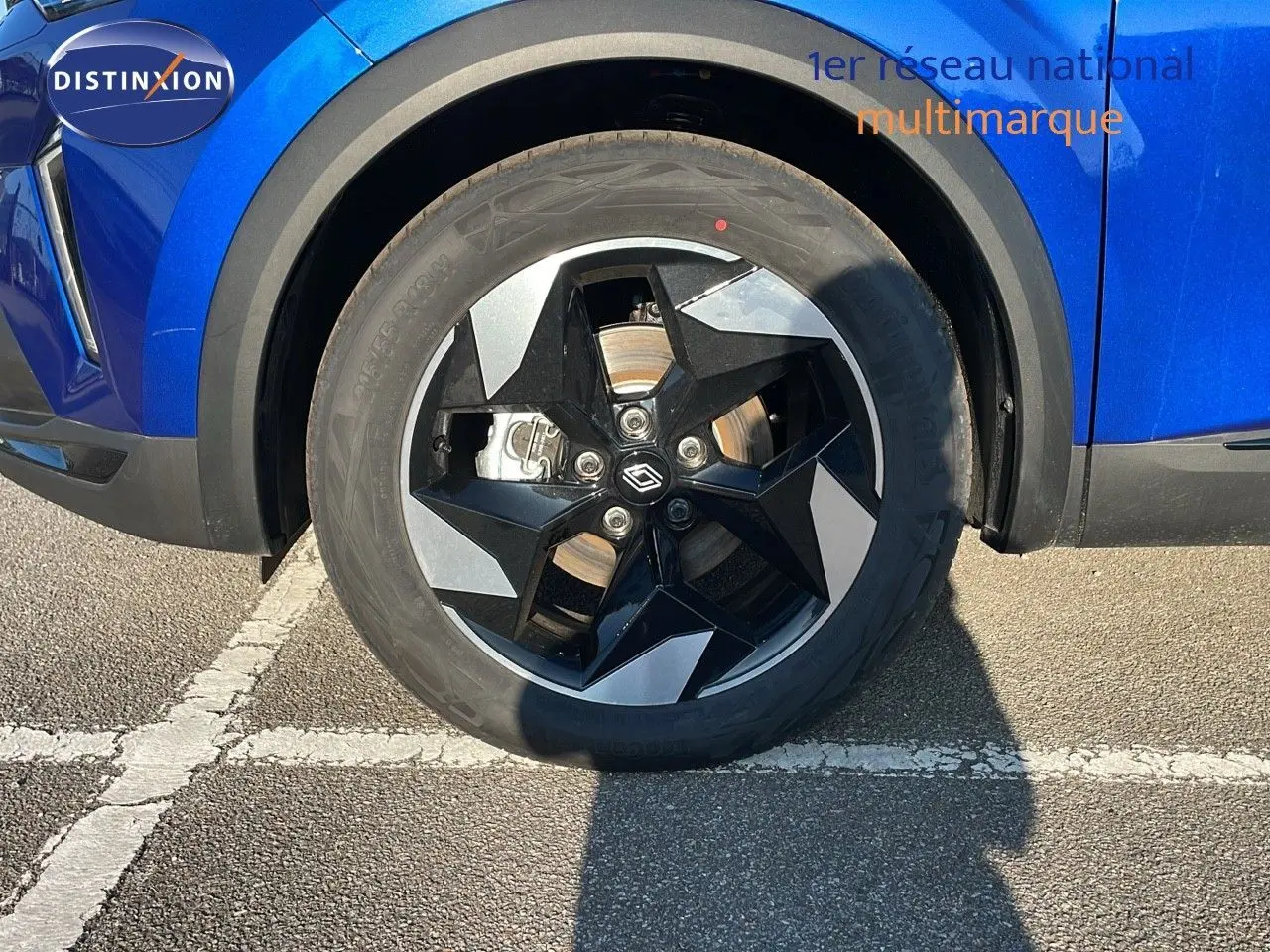 Gros plan sur la roue avant gauche du Renault Captur bleu Iron Metal avec jante noire et grise au design étoilé.