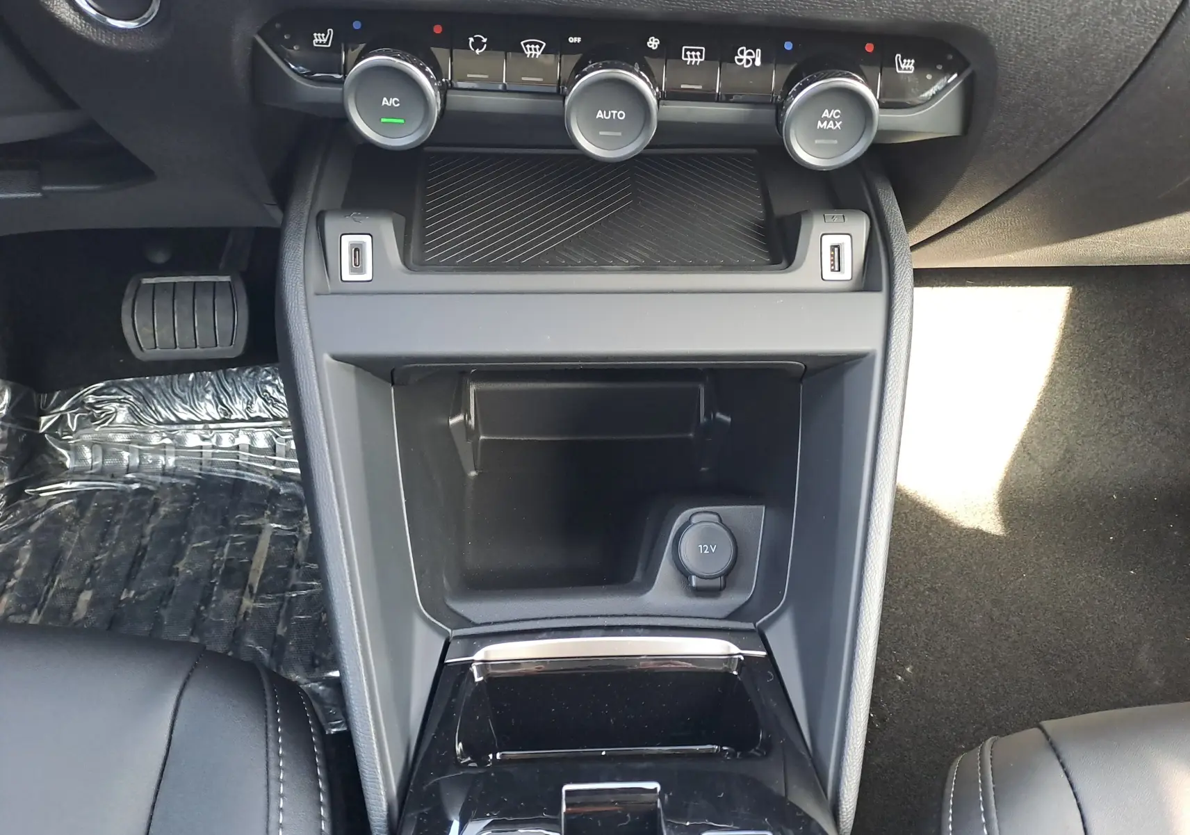 Vue rapprochée de la console centrale du Citroën C4 hybride 2025, avec commandes climatisation et prise 12V visibles.