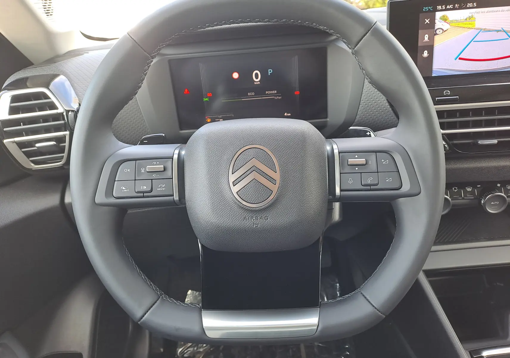 Vue rapprochée du volant multifonction noir de la Citroën C4 hybride 2025 avec tableau de bord digital et écran d'aide au stationnement.