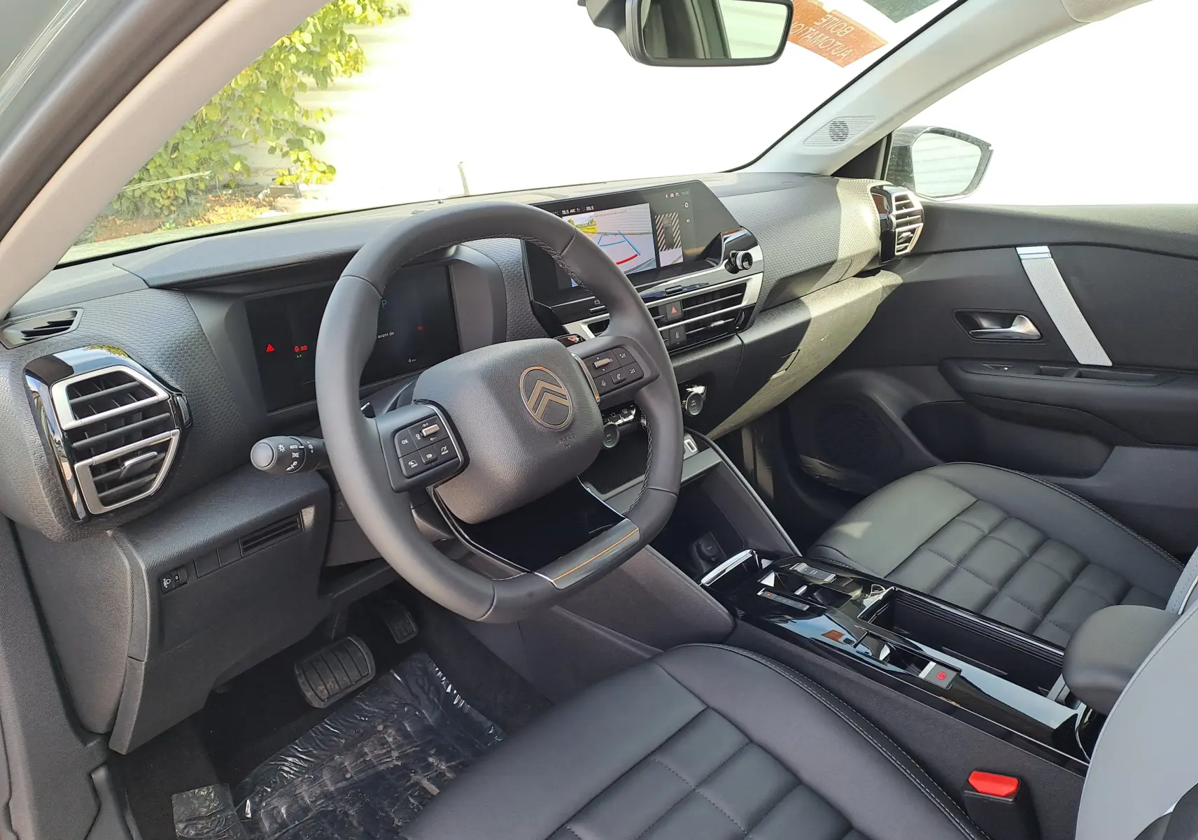 Vue intérieure côté conducteur de la Citroën C4 hybride 2025, avec tableau de bord moderne et sièges en cuir noir.