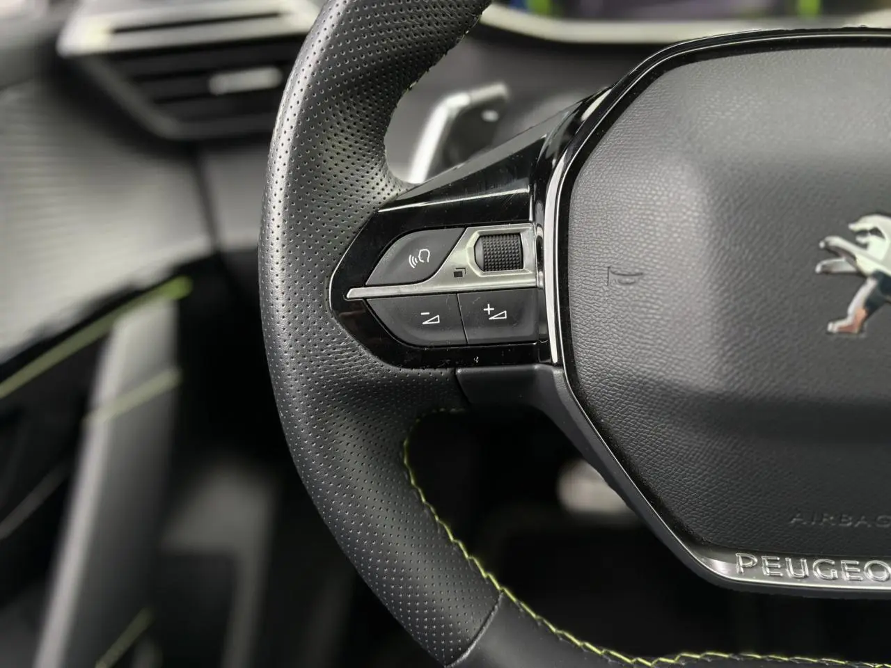 Gros plan sur le volant cuir noir perforé avec surpiqûres vertes et logo Peugeot au centre du Peugeot 208 GT.