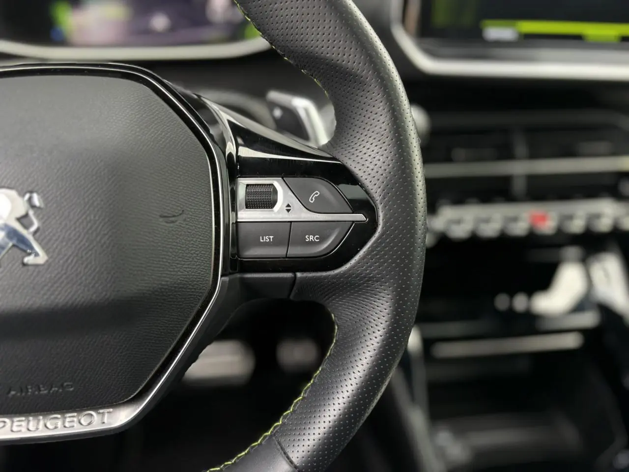 Gros plan sur le volant cuir noir perforé avec surpiqûres vertes et commandes multimédia de la Peugeot 208 GT 2023.
