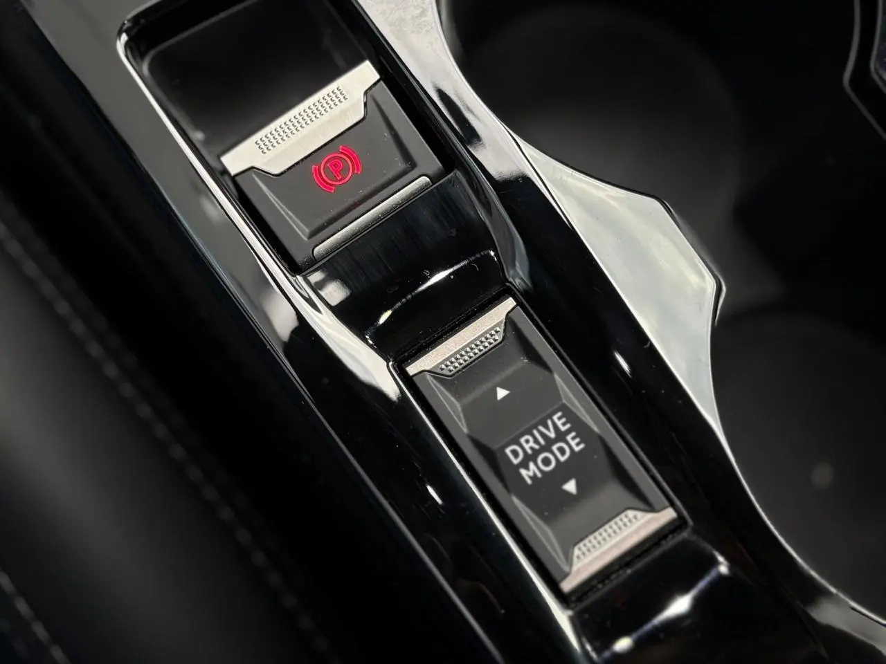 Gros plan sur la console centrale noire brillante du Peugeot 208 GT 2023 avec bouton frein à main électrique et sélection mode de conduite.