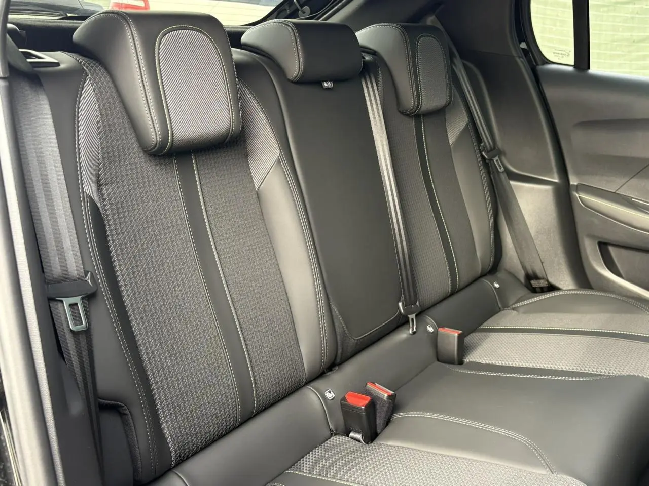 Vue rapprochée de la banquette arrière noire avec surpiqûres blanches et ceintures de sécurité dans une Peugeot 208 2023.