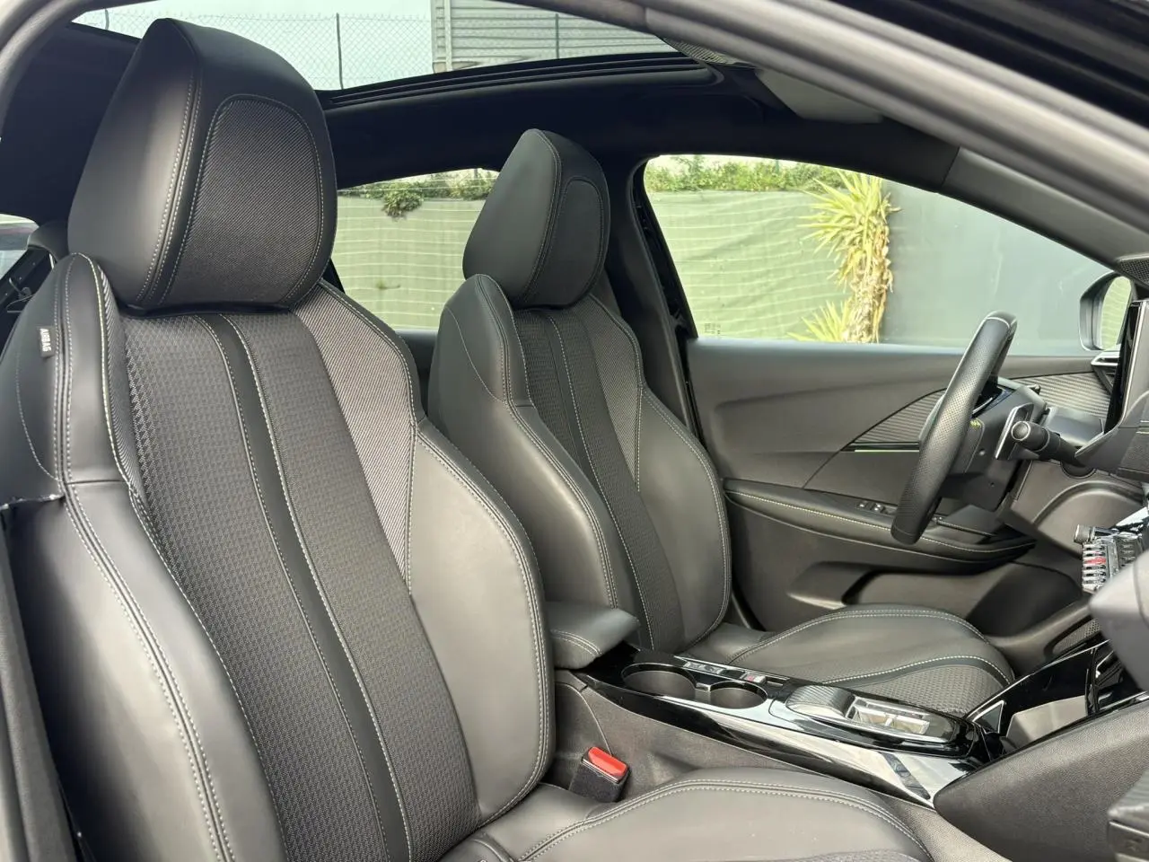 Vue intérieure côté droit de la Peugeot 208 GT 2023 avec sièges sport noirs et toit panoramique ouvert.