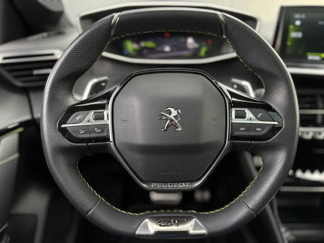 Gros plan sur le volant cuir noir avec surpiqûres vertes et logo Peugeot GT du tableau de bord de la 208 Noir Perla.