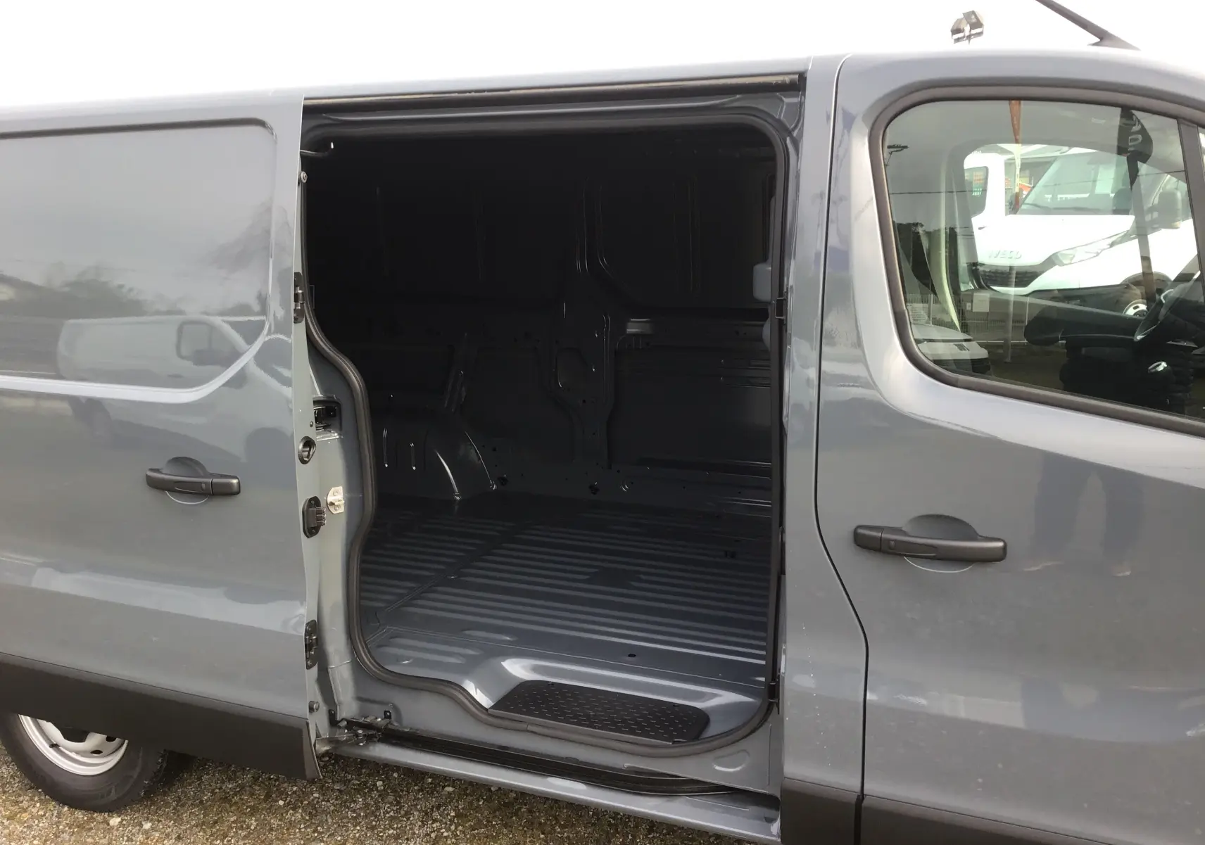 Vue latérale gauche d’un Renault Trafic Fourgon gris urbain 2025 avec porte coulissante ouverte montrant l’espace de chargement vide.