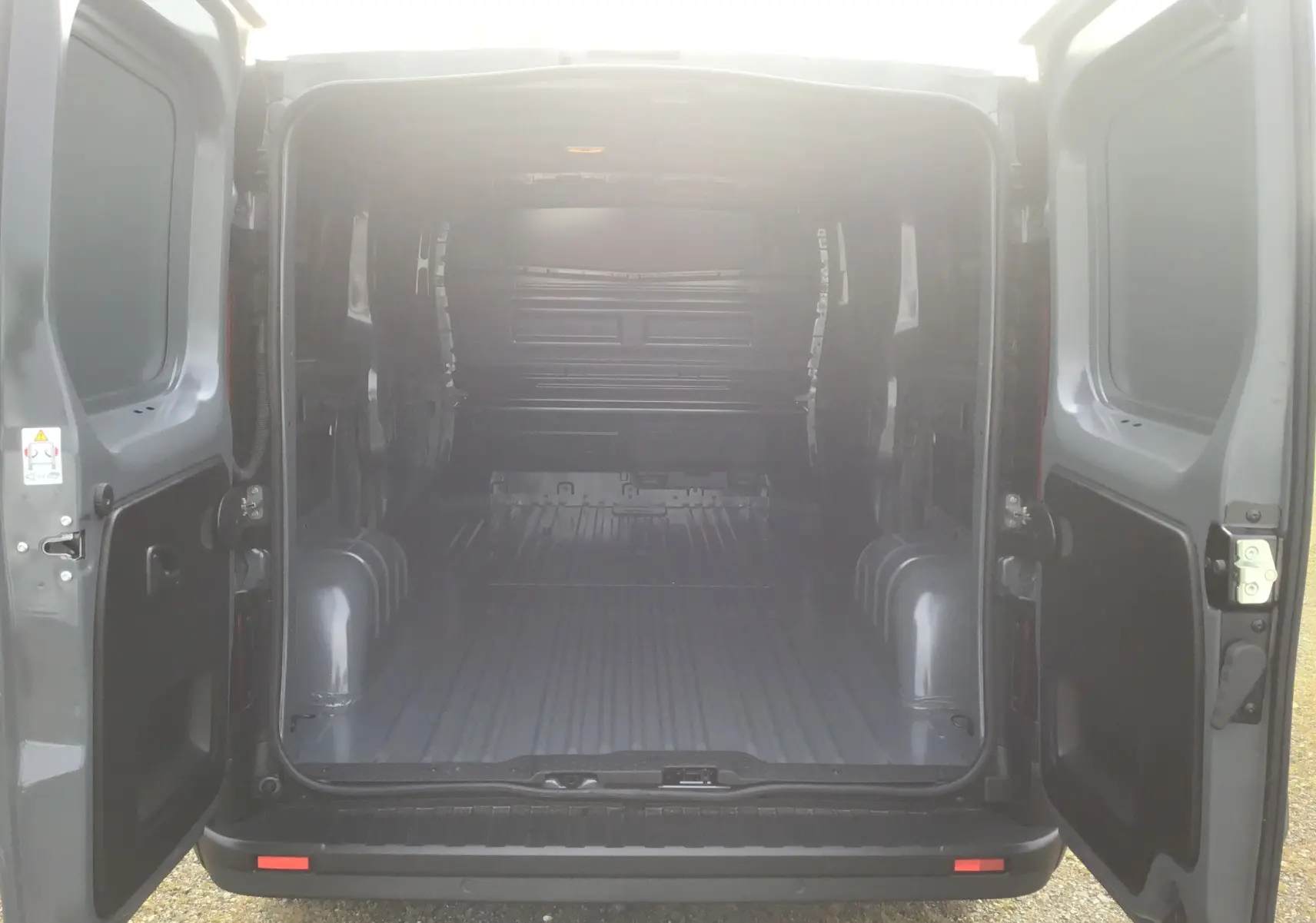 Vue arrière du Renault Trafic Fourgon gris urbain 2025 avec portes ouvertes montrant l’espace de chargement vide.