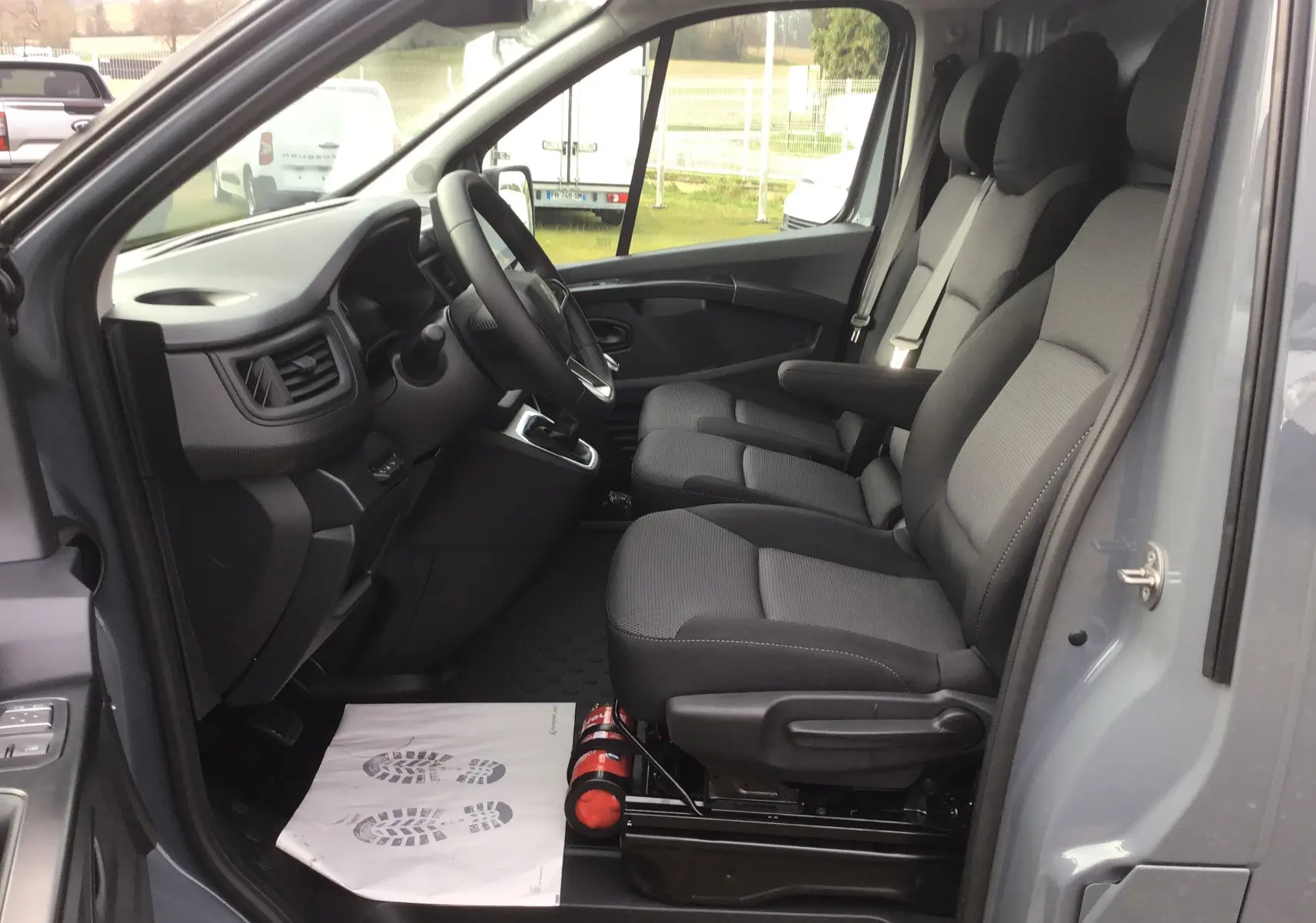 Vue intérieure côté conducteur du Renault Trafic Fourgon gris urbain 2025, montrant les sièges avant et le tableau de bord.