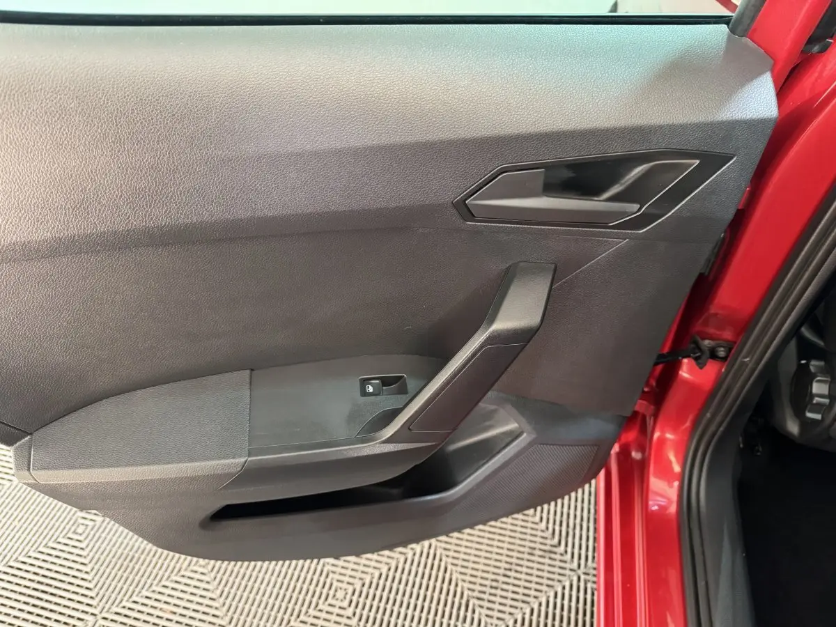 Vue rapprochée de la porte avant gauche rouge de la SEAT IBIZA 1.0 TSI 110 FR avec poignée et commande de vitre noire.