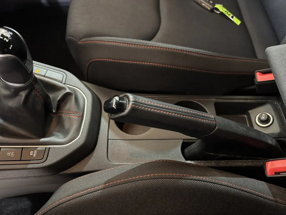 Gros plan sur frein à main et levier de vitesses manuelle avec surpiqûres rouges dans l'habitacle d'une SEAT Ibiza rouge 2024.