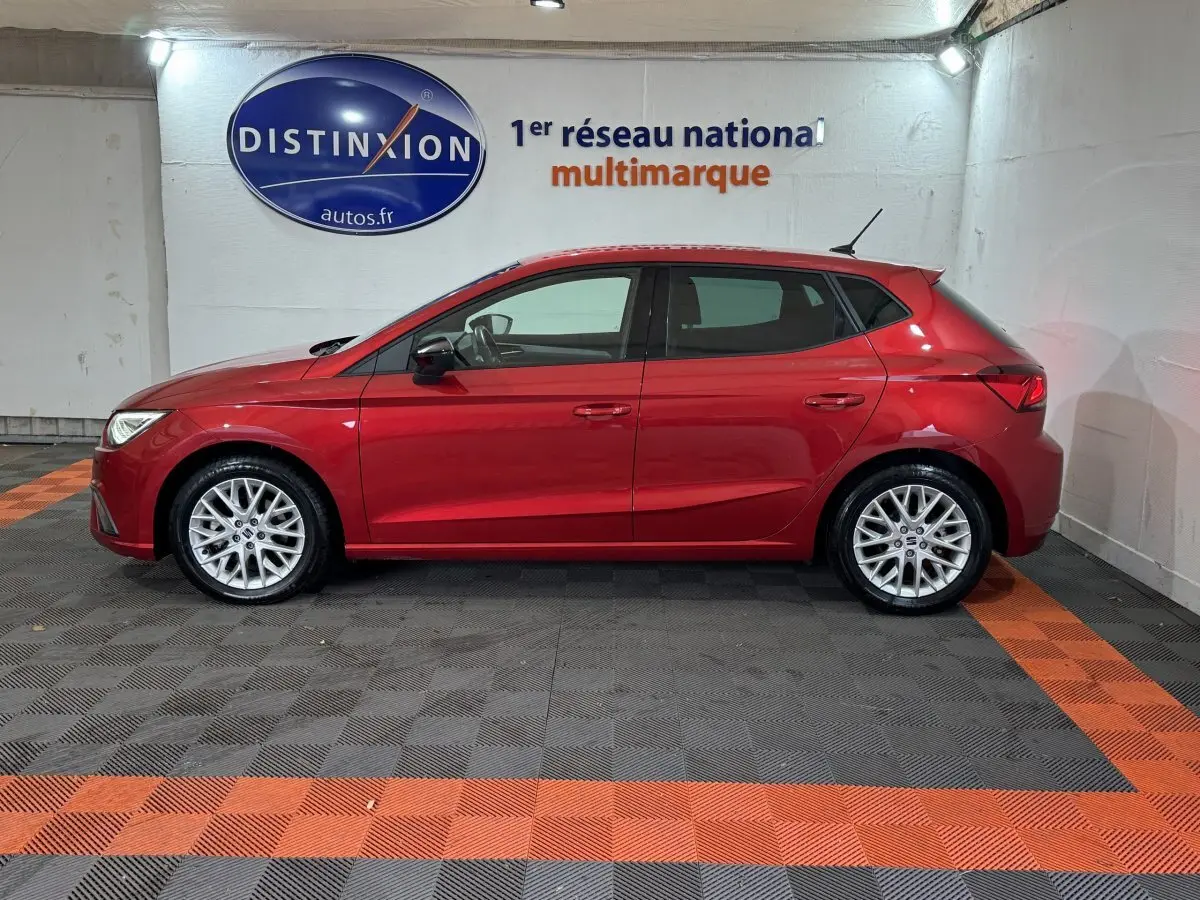 Profil côté gauche d'une SEAT IBIZA 1.0 TSI 110 FR rouge, en intérieur sur sol à damiers gris et orange.