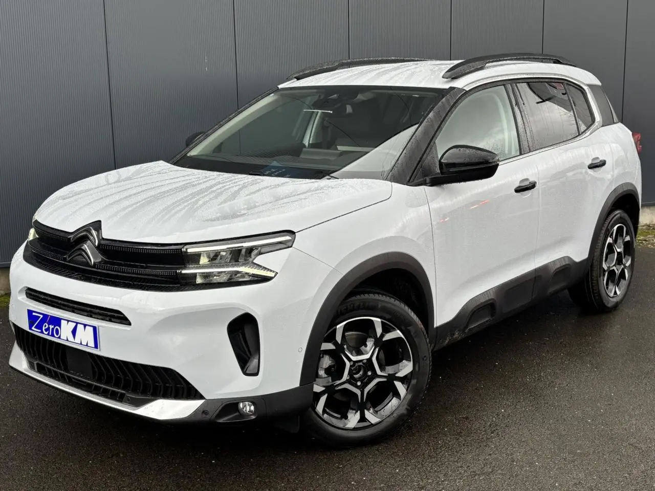 Vue 3/4 avant droit d'un Citroën C5 Aircross blanc Okénite avec jantes alliage 18'' bi-ton et barres de toit noires.