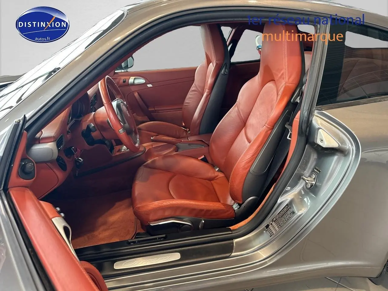 Intérieur cuir rouge vu côté conducteur d'une Porsche 911 (997) Carrera PDK gris, avec tableau de bord et sièges sport visibles.