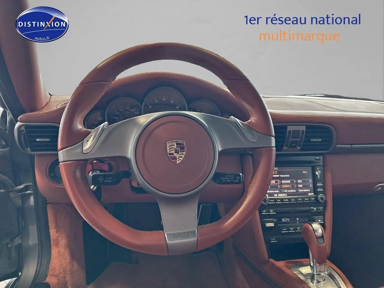 Intérieur d'une Porsche 911 (997) carrera pdk 2009, vue centrée sur le volant cuir marron et la console centrale.