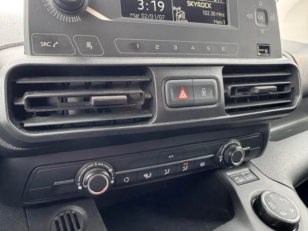 Gros plan sur la console centrale noire du Citroën Berlingo blanc, montrant les aérateurs et commandes de climatisation.