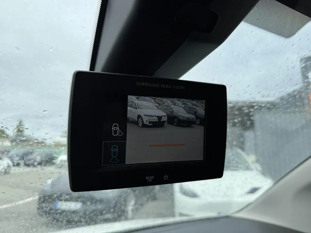 Écran de caméra de recul dans un Citroën Berlingo blanc, vue intérieure sous pluie avec voitures en arrière-plan.