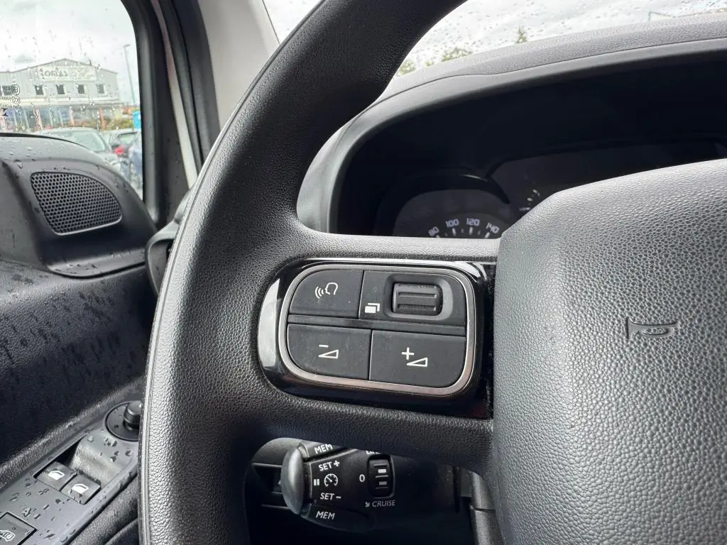 Gros plan sur les commandes au volant noir du Citroën Berlingo blanc, avec vue partielle du tableau de bord et porte côté gauche.