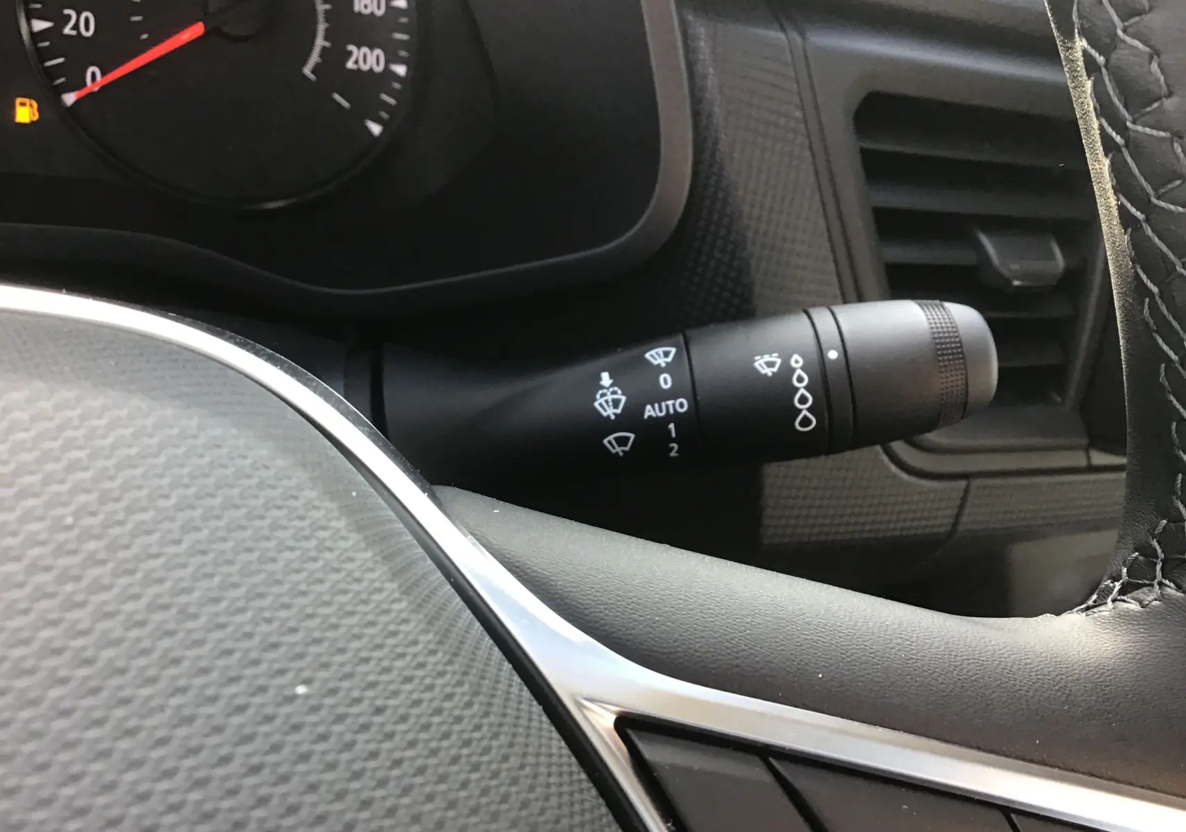 Gros plan sur la manette d’essuie-glace à droite du volant dans l’habitacle du Renault Trafic blanc, tableau de bord partiellement visible.