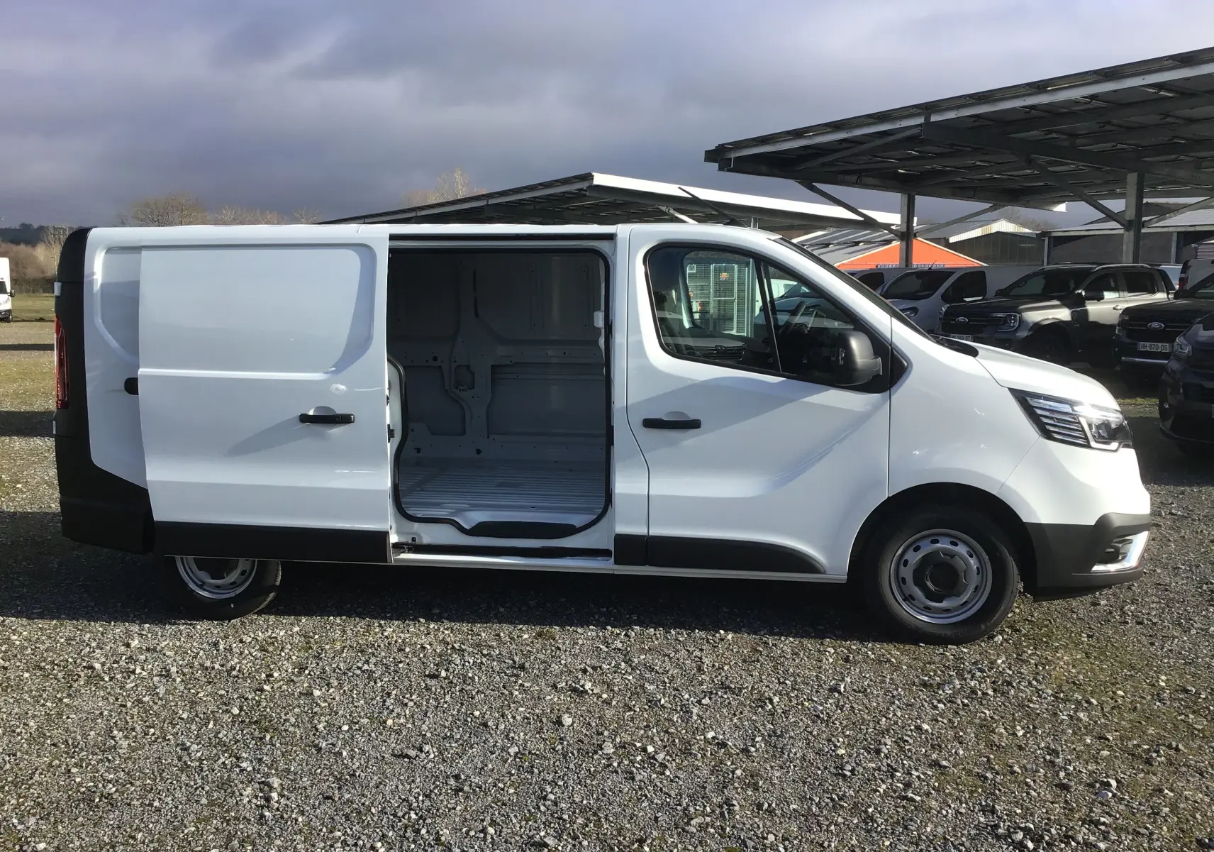 Vue de profil côté droit d’un Renault Trafic Fourgon blanc 2025 avec porte latérale coulissante ouverte montrant l’espace de chargement.