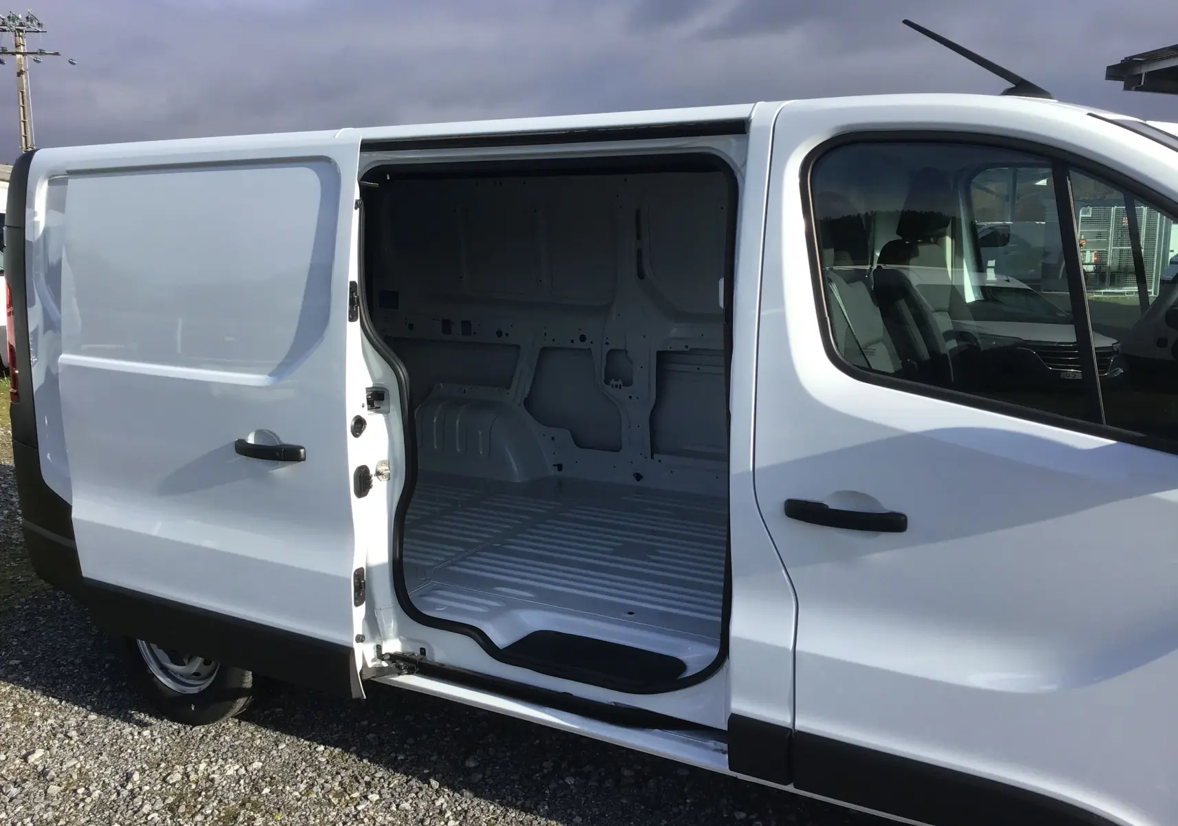 Vue latérale droite d’un Renault Trafic Fourgon blanc 2025 avec porte coulissante ouverte dévoilant l’espace de chargement vide.