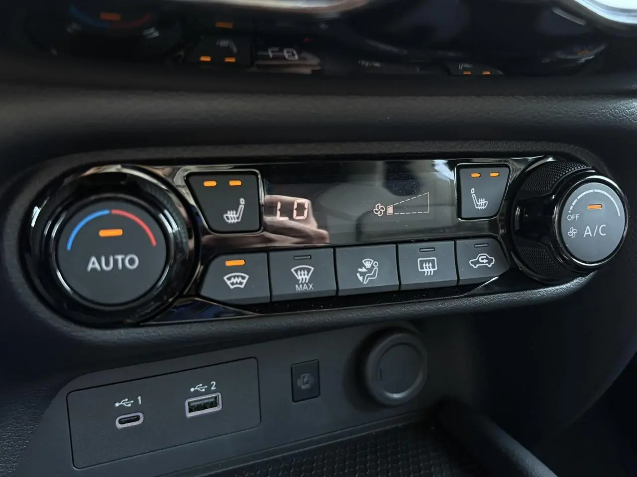 Gros plan sur la console de climatisation noire du Nissan Juke 2024 avec commandes chauffantes et ventilation automatique.