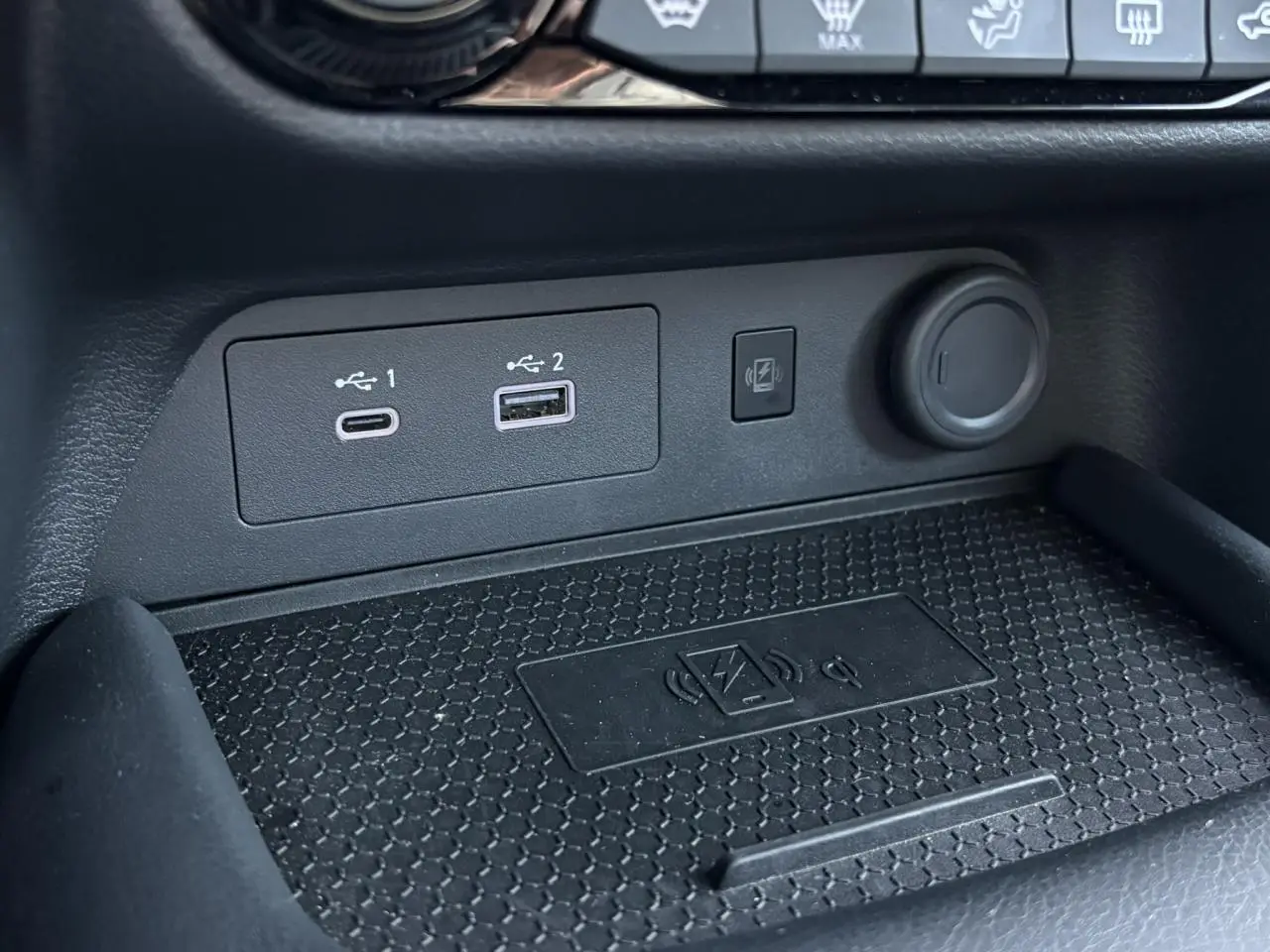 Gros plan sur la console centrale du Nissan Juke 2024, montrant les ports USB, prise 12V et chargeur sans fil.