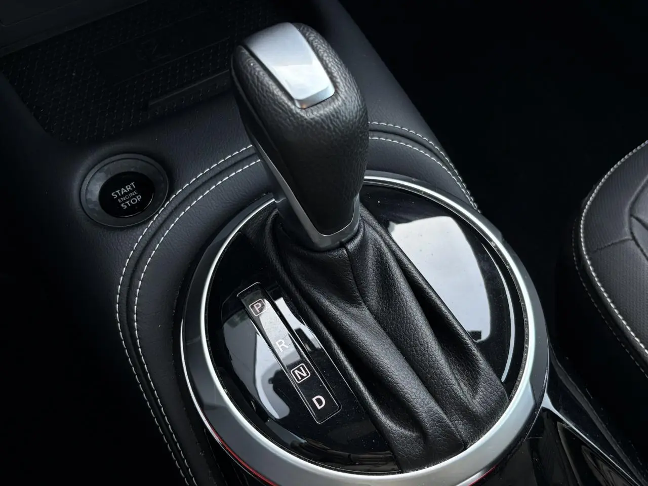 Gros plan sur le levier de vitesses automatique noir avec surpiqûres blanches dans l’habitacle du Nissan Juke 2024.