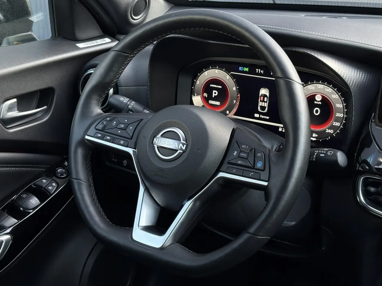 Vue rapprochée du volant noir et du combiné d'instruments digital du Nissan Juke 2024 côté conducteur.