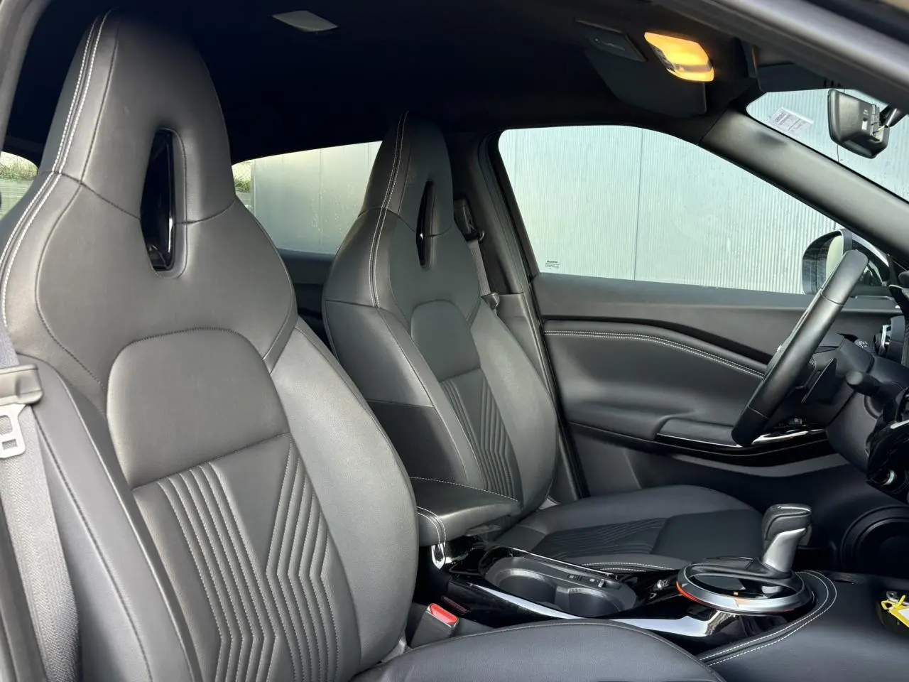 Vue intérieure côté avant droit du Nissan Juke 2024 avec sièges sport noirs et console centrale brillante.