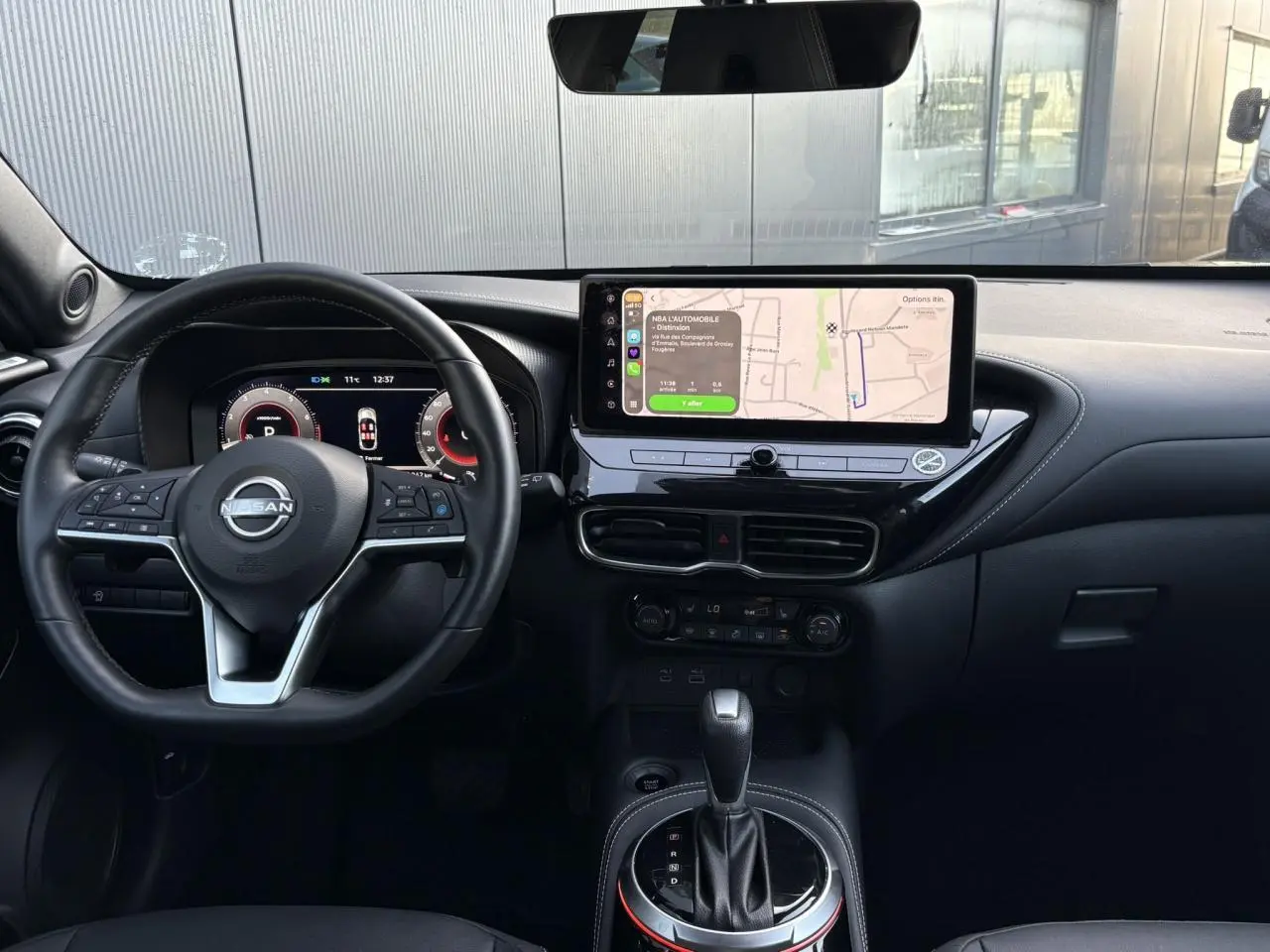 Vue intérieure frontale du Nissan Juke 2024 avec tableau de bord noir, écran tactile central et volant multifonction.