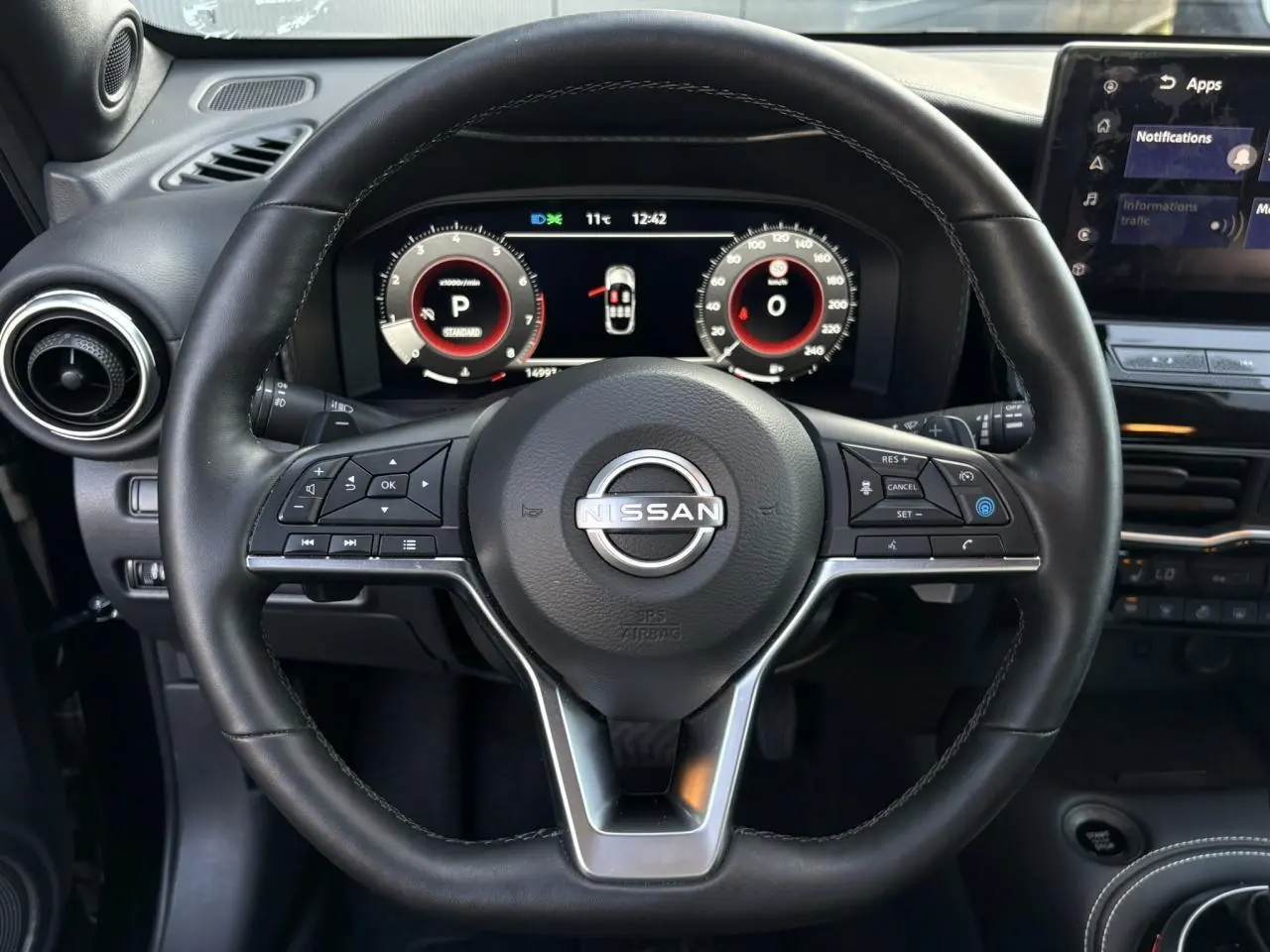 Vue rapprochée du volant noir du Nissan Juke 2024 avec commandes multifonctions et combiné digital lumineux.