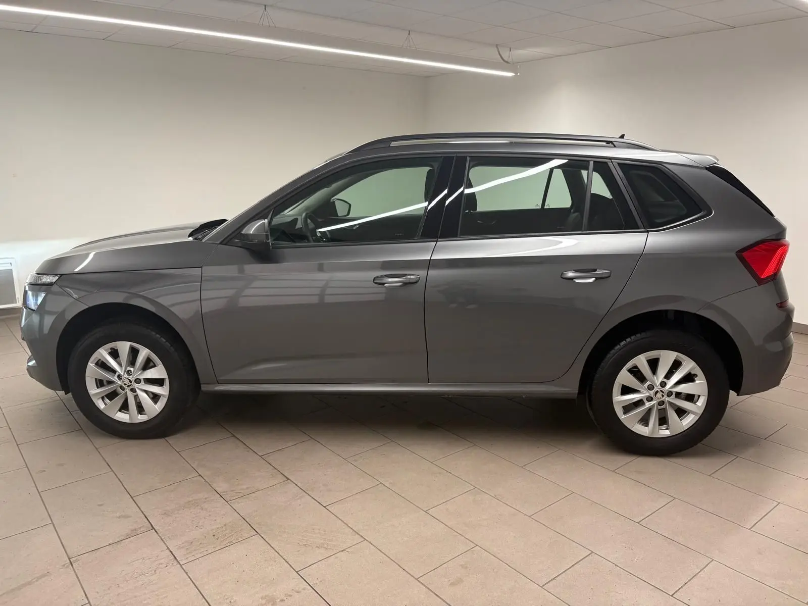Vue de profil côté gauche d'un Skoda Kamiq 2023 gris graphite métallisé avec jantes alliage en intérieur neutre.