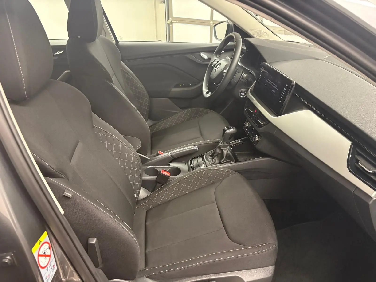 Intérieur avant droit du Skoda Kamiq 2023 gris graphite, sièges tissu noir avec surpiqûres et tableau de bord moderne.